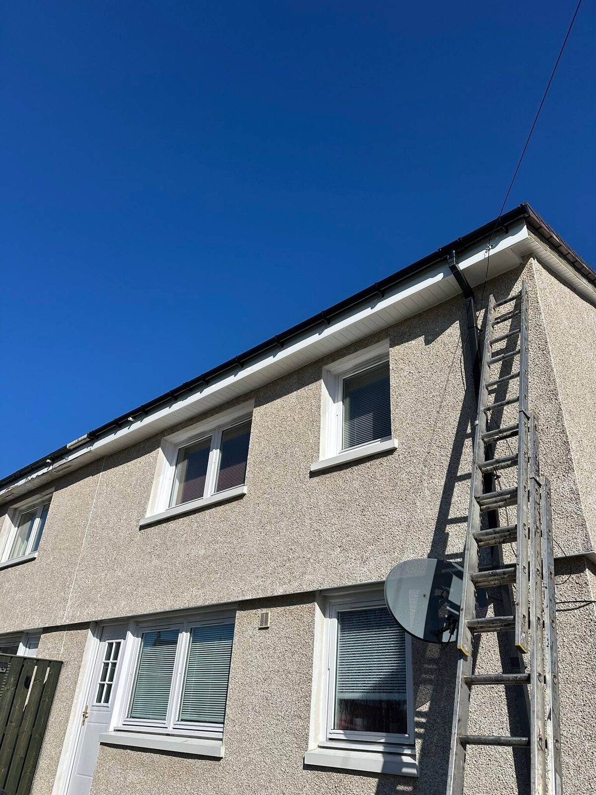 The back of a house with a new white soffit and fascia, plus a black gutter and downpipe, under a deep blue sky