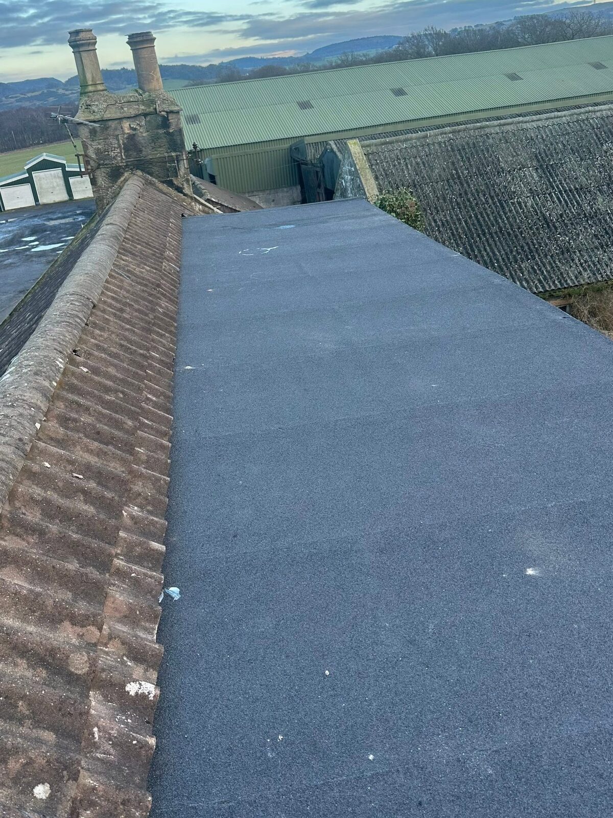 A flat roof finished in a blue-grey mineral cap sheet at dusk