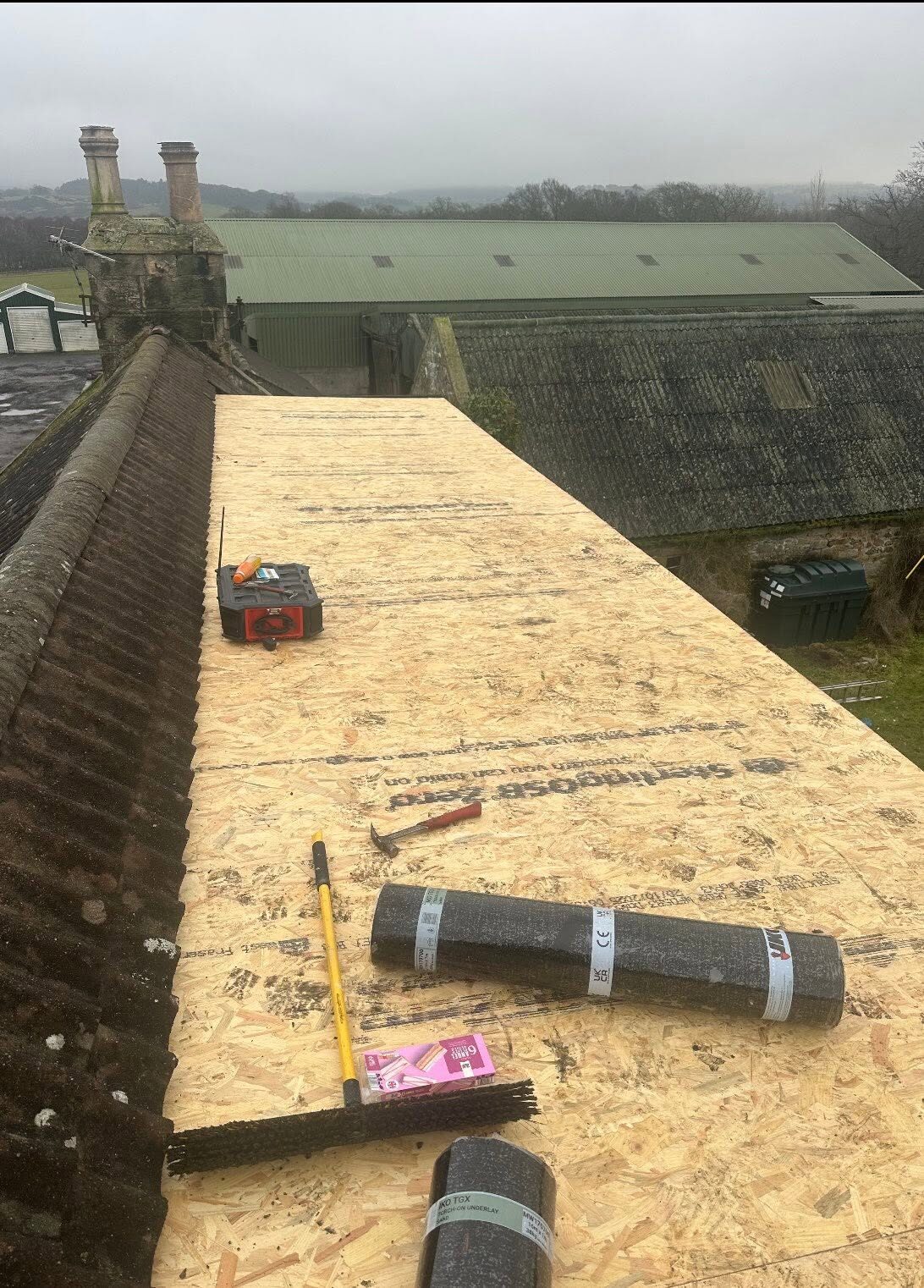 Long flat roof re-boarded in new timber sheets beside a tiled roof, with rolls of felt ready
