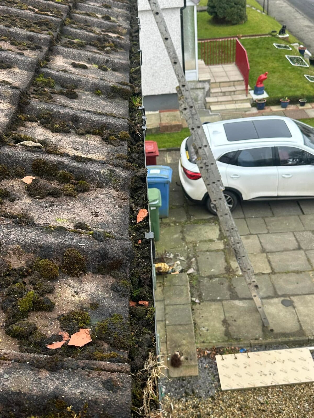 Gutter along concrete roof tiles choked with moss and grass