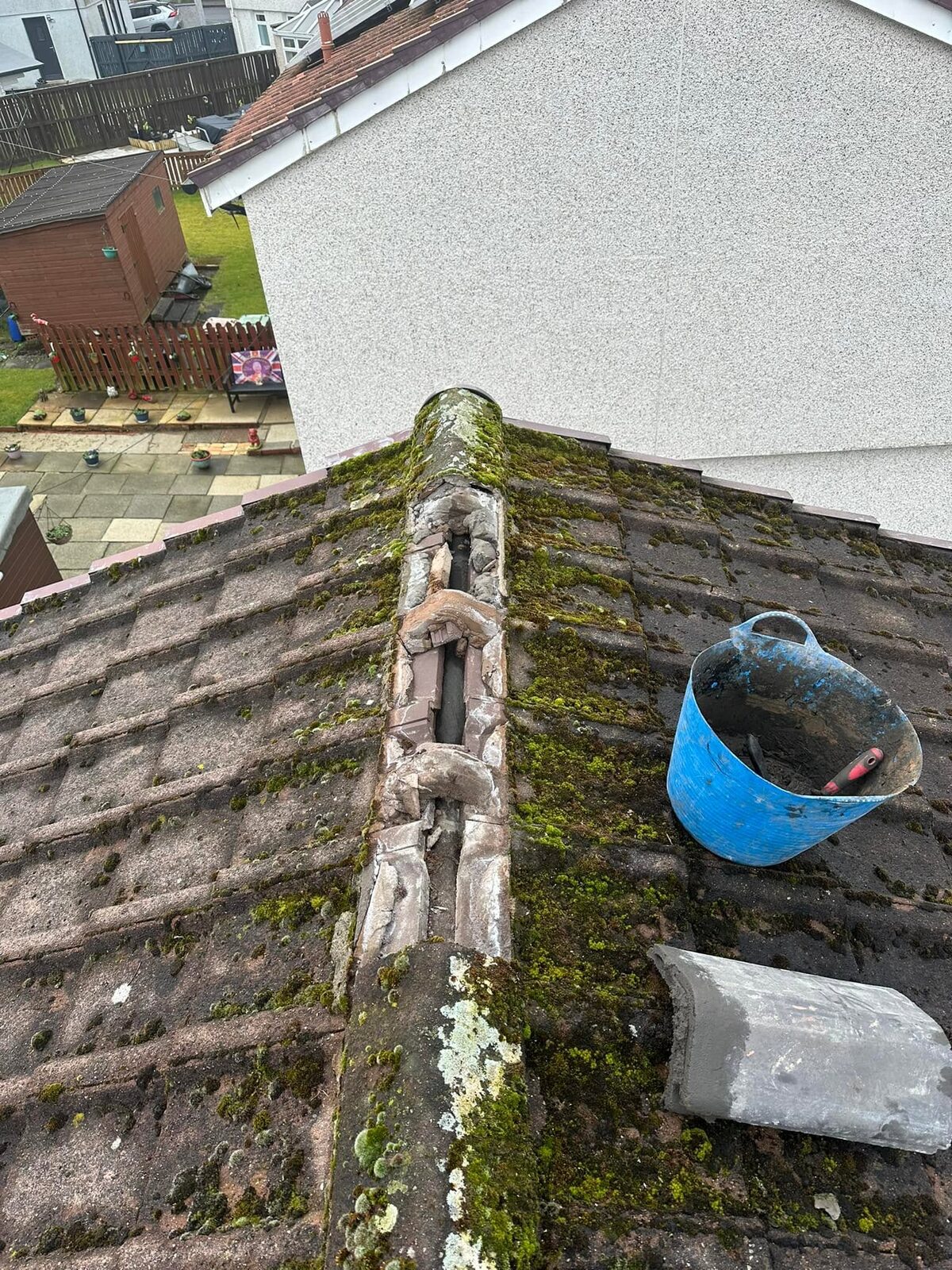 Ridge on a mossy tiled roof with two ridge tiles off and the old bedding broken out