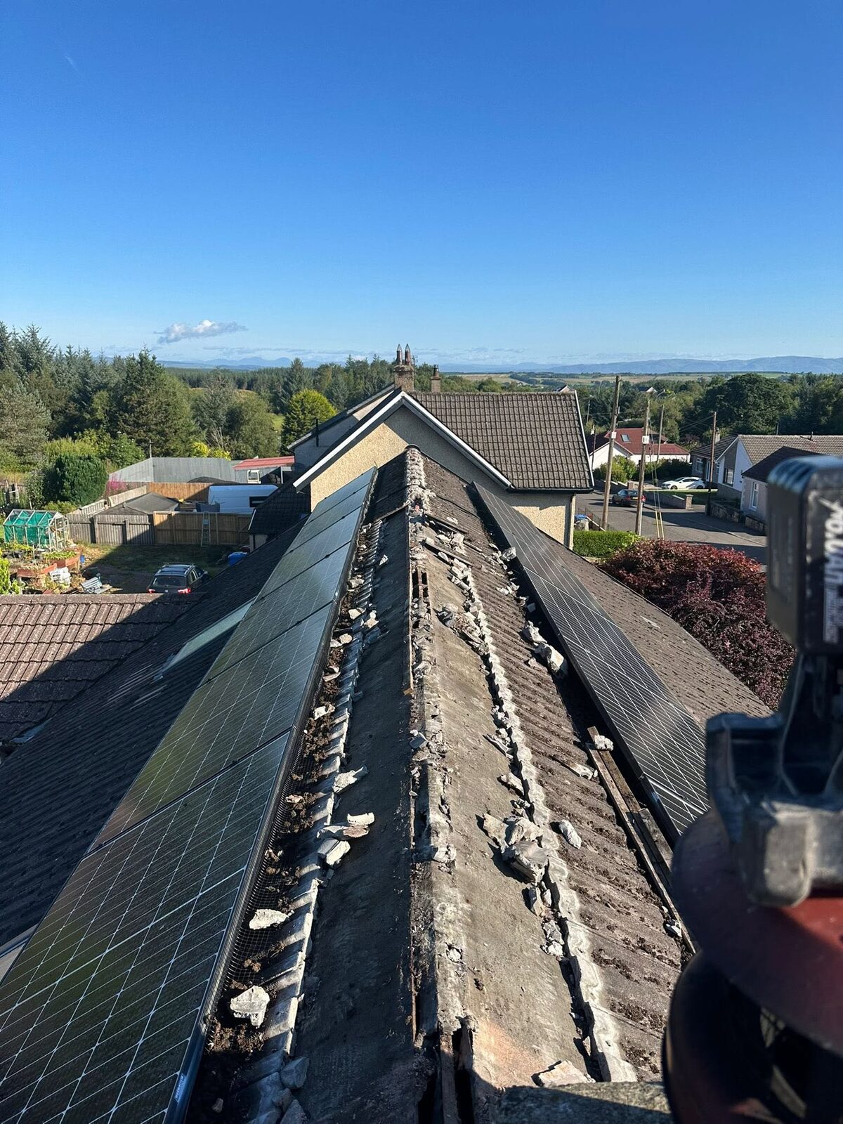 Long tiled ridge between two solar panel arrays with the old ridge tiles removed and broken mortar along the top