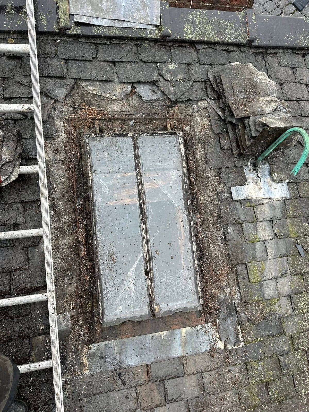 Old metal-framed rooflight in a slate roof with the slates stripped round it