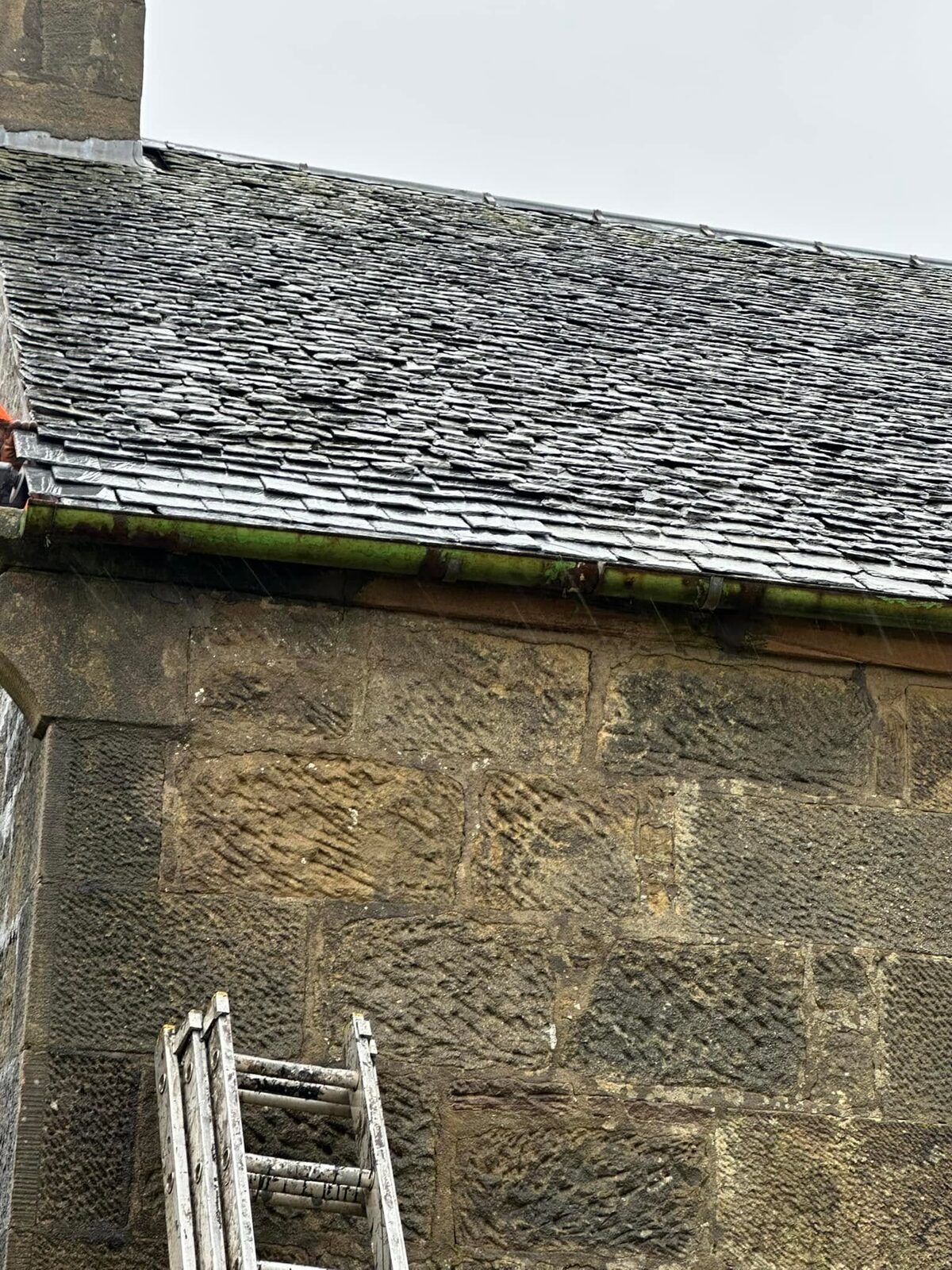 Sandstone building with an old Scotch slate roof and a green cast-iron gutter